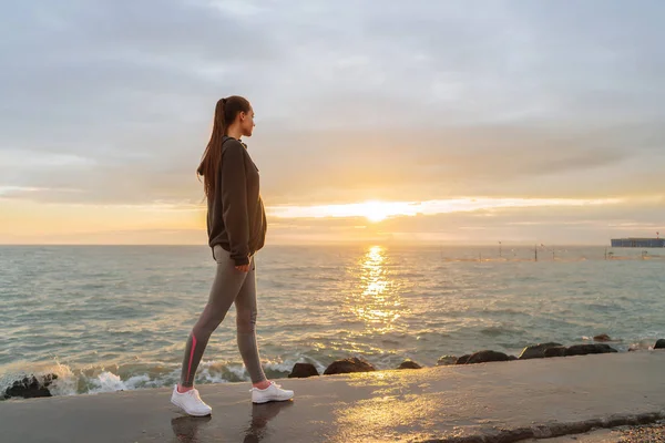slender girl in sportswear is engaged in jogging at the sea at sunset, wants to lose weight