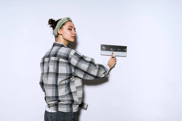Een jong meisje in een plaid shirt nivelleren van een muur met een spatel, doen reparaties in het appartement — Stockfoto