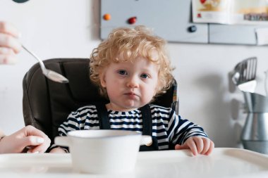Onu yararlı yulaf lapası, beslenme anne mutfak, bir sandalyede oturan kıvırcık küçük oğlu Aile yemeği