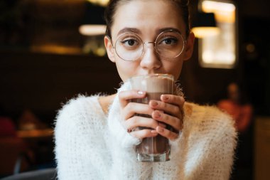 Gözlüklü Şirin genç kız öğrenci bir kafede lezzetli kahve içer