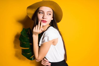 güzel uzun saçlı kız modeli trendy şapkalı bir yaprak yeşil ve turuncu bir arka plan üzerinde poz tutar