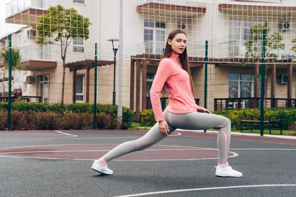Chica atlética segura amasa los músculos de las piernas antes de entrenar en el campo de deportes al aire libre — Foto de Stock