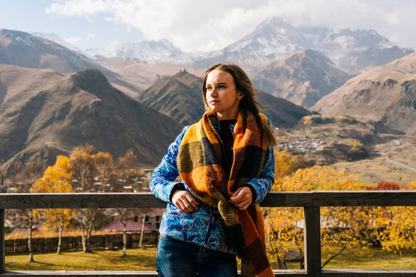 Menina agradável em uma jaqueta quente viaja, fica em um fundo de majestosas montanhas altas, apreciando o cenário — Fotografia de Stock