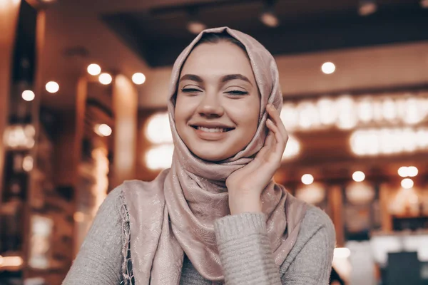 Tertawa gadis Arab muda dengan kerudung duduk di sebuah restoran oriental yang indah, menunggu makanannya — Stok Foto