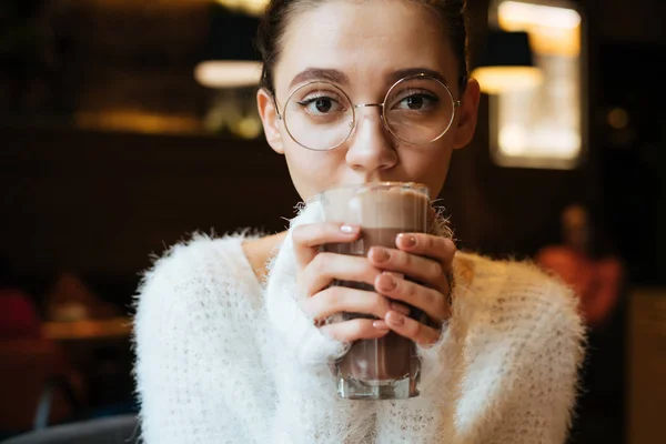 Милий молода дівчина студент в окулярах п'є смачний латте в кафе — стокове фото