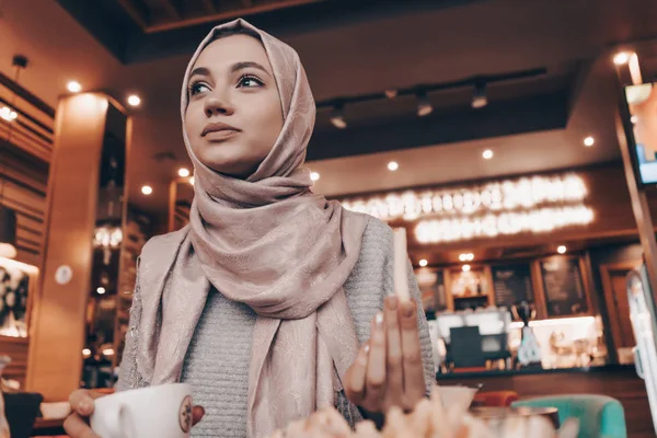 Agradable chica musulmana en hijab almorzando en acogedora cafetería y sonriendo — Foto de Stock