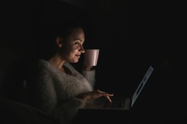 Genç kız yatakta gece geç saatlerde, oturup onu laptop komik dizi izlemek gülümseyen — Stok fotoğraf