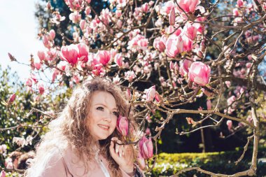 bir çiçek Pembe Manolya yanında poz, gülen ve sıcaklığına zevk kıvırcık mutlu genç kadın