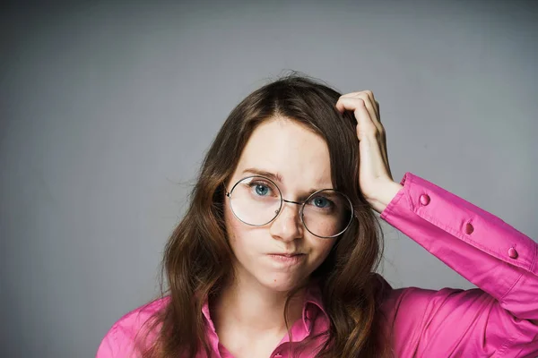 Jovem menina de olhos azuis pensativo em uma camisa rosa e óculos olha para a câmera — Fotografia de Stock