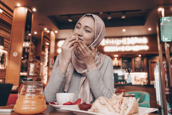 Aranyos arab lány a fejkendő a fején finom étkezés egy keleti kávézóban — Stock Fotó