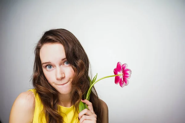 Schöne junge blauäugige Frau in einem gelben Kleid hält eine duftende rosa Blume in der Hand und blickt in die Kamera — Stockfoto