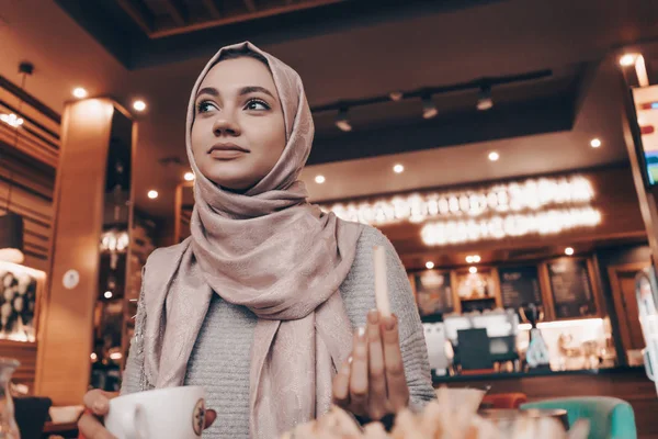 Une jolie fille musulmane en hijab s'assoit dans un restaurant et mange un délicieux repas, souriant — Photo