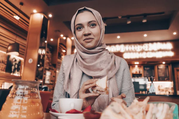 Schöne arabische Mädchen mit Kopftuch auf dem Kopf speist in einem gemütlichen Restaurant, lächelnd — Stockfoto