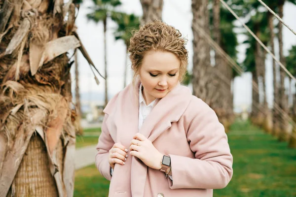 Beautiful elegant girl in a trendy pink coat posing in a green spring park — Stock Photo, Image