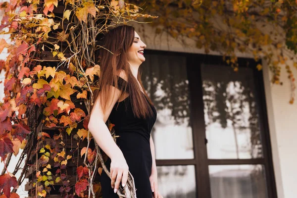 Lycklig rik kvinna med långt hår och i en svart klänning vila och poserar i hennes trädgård — Stockfoto