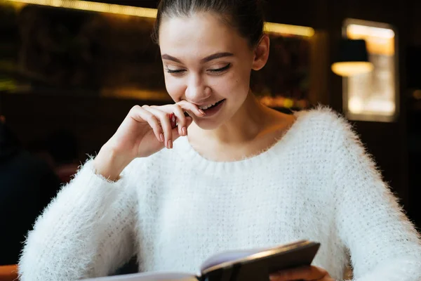 Красивая улыбающаяся девочка студентка в белом свитере читает лекции, улыбается, сидит в кафе — стоковое фото