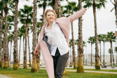 mutlu güzel kız pembe bir ceket uzun boylu yeşil palms yanındaki parkta yürüyor