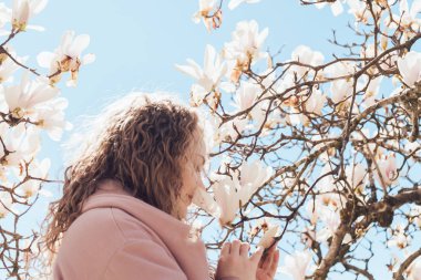 kıvırcık çekici kadın mavi gökyüzü altında bir parkta bir aromatik çiçek açan Manolya koklama