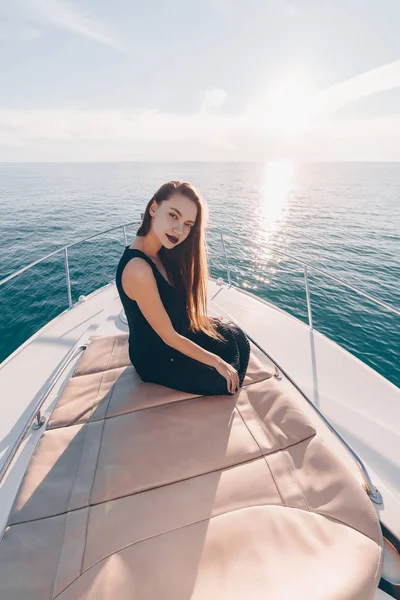 Ein attraktives langhaariges Mädchen mit schwarzem Lippenstift und schwarzer Sommerkleidung sitzt auf ihrer weißen Jacht und genießt die Seereise — Stockfoto