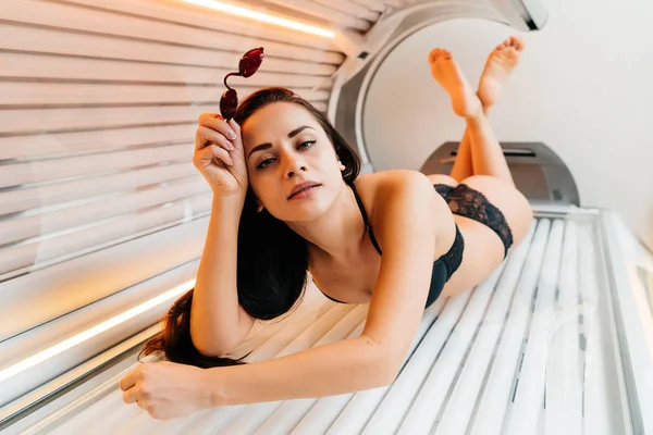 Atraente delgado morena menina encontra-se em um solário horizontal, quer uma bela pele bronzeada — Fotografia de Stock