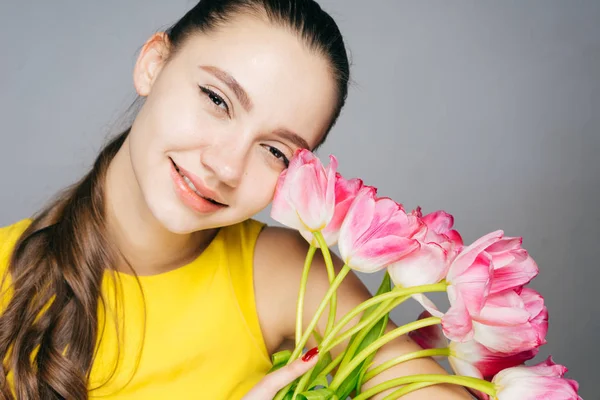 Attractive young girl in a yellow dress enjoying the spring, holding fragrant flowers and smiling — Stock Photo, Image