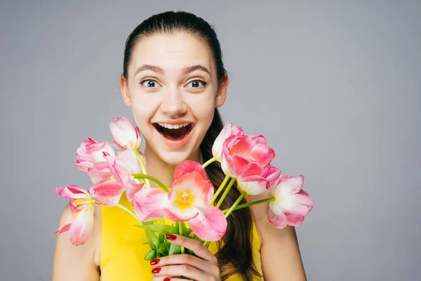 Šťastné překvapení dívka v žlutých šatech drží růžové květy, jaro a teplo — Stock fotografie