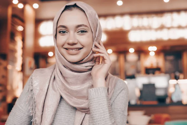 Vacker muslimsk flicka med en huvudduk som sitter i en mysig restaurang, ler och väntar på sin mat — Stockfoto