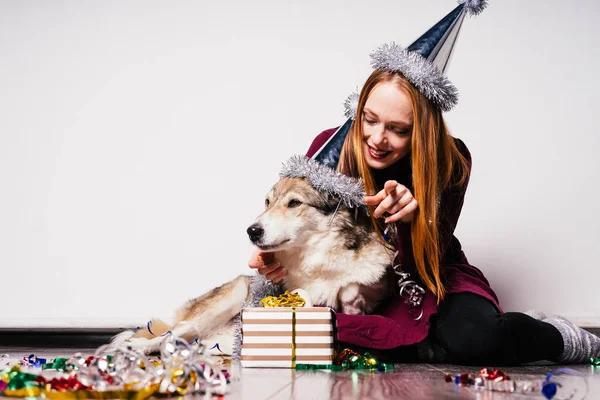 Happy red-haired girl in a cap playing with her dog, celebrating a new year and christmas — Stock Photo, Image