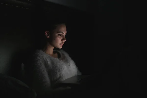 Giovane ragazza freelance stanca seduta a letto a tarda notte e al lavoro sul suo portatile — Foto Stock