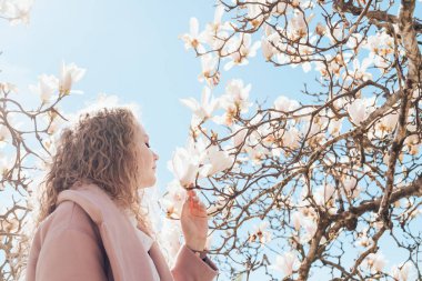 güneş ışığı altında bir parkta blooming Manolya kokusu tadını paltolu kıvırcık çekici kız