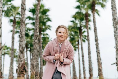 şık bir ceket neşeli zarif kız yanındaki uzun boylu palmiye ağaçları yeşil park boyunca yürür ve eğlence var