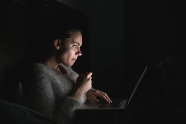 gece yatakta karanlıkta oturmuş ve laptop bir film izlerken ciddi genç kız