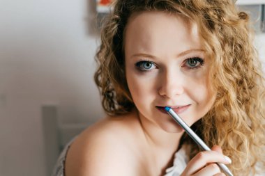 güzel kıvırcık genç kadın mutfakta bir kalem tutan ve kameraya bakarak oturuyordu