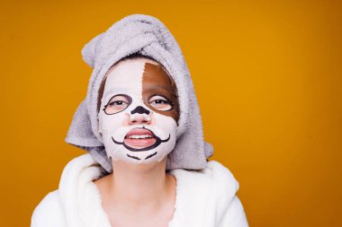 Genç kız başında bir duş sonra bir havlu ile kamera ve gülümsüyor, yüzünde bir nemlendirici maske ile bir köpeğin yüz görünüyor