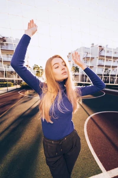 Bela jovem modelo em um suéter posando em um campo de esportes nos raios do sol da manhã — Fotografia de Stock
