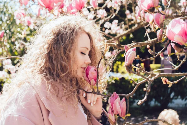 Chica dulce rizado huele una magnolia floreciente en el parque, disfruta del clima cálido de primavera — Foto de Stock