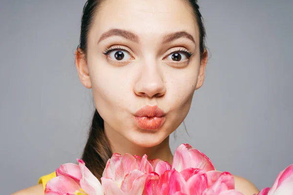 Pembe çiçekler holding, kameraya bakıyor ve poz komik genç güzel kız — Stok fotoğraf