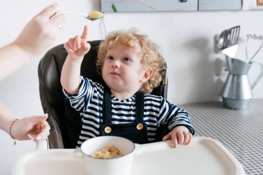 kıvırcık küçük çocuk mutfakta bir sandalyeye oturur, annesi ile sağlıklı yemek yiyor