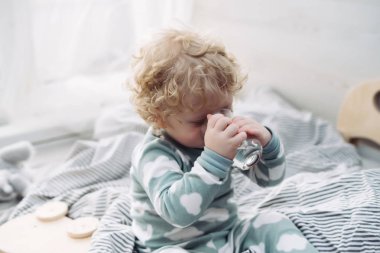 kıvırcık küçük çocuk şirin pijamaları yatağın üstüne oturur ve suyu içer