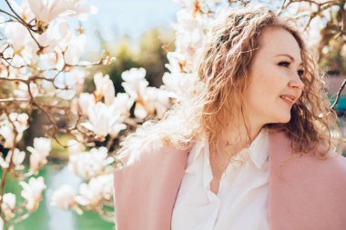 çiçek açan Manolya yanındaki bir park ve bir su birikintisi içinde poz zarif kıvırcık saçlı kız