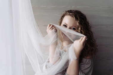 bir beyaz perde tutan Pencerenin kenarında oturan genç kıvırcık kız gülerek