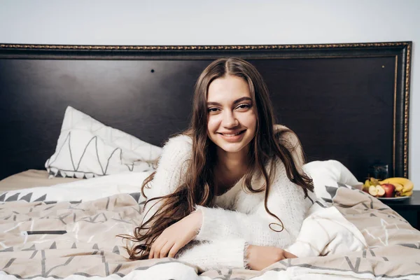 Schöne langhaarige Mädchen liegt spät in der Nacht im Bett, ruht nach einem Arbeitstag und lächelt — Stockfoto