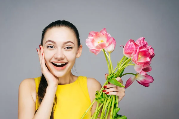 Het vreugdevolle verrast meisje in een gele jurk is genieten van de warmte en in de lente, inhoudende een boeket geurende bloemen — Stockfoto