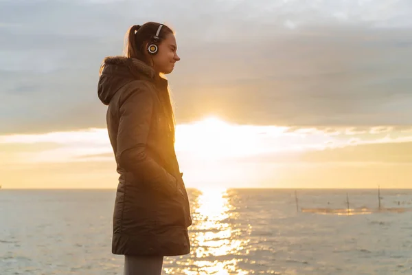 peaceful happy girl walks by the sea at sunset and listens to music on headphones