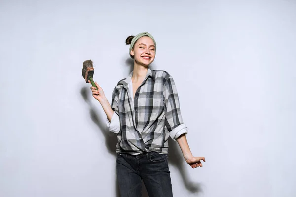 Gelukkig lacht lachend meisje verf de muur met een borstel in haar appartement, — Stockfoto
