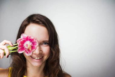 gülümseyen ve kameraya bakarak yüz yakınındaki bir kokulu pembe çiçek tutan güzel genç kadın