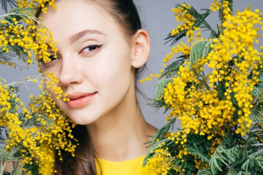 güzel genç kız güzel kokulu Mimoza tutan bir sarı elbiseli poz ve kameraya, seyir