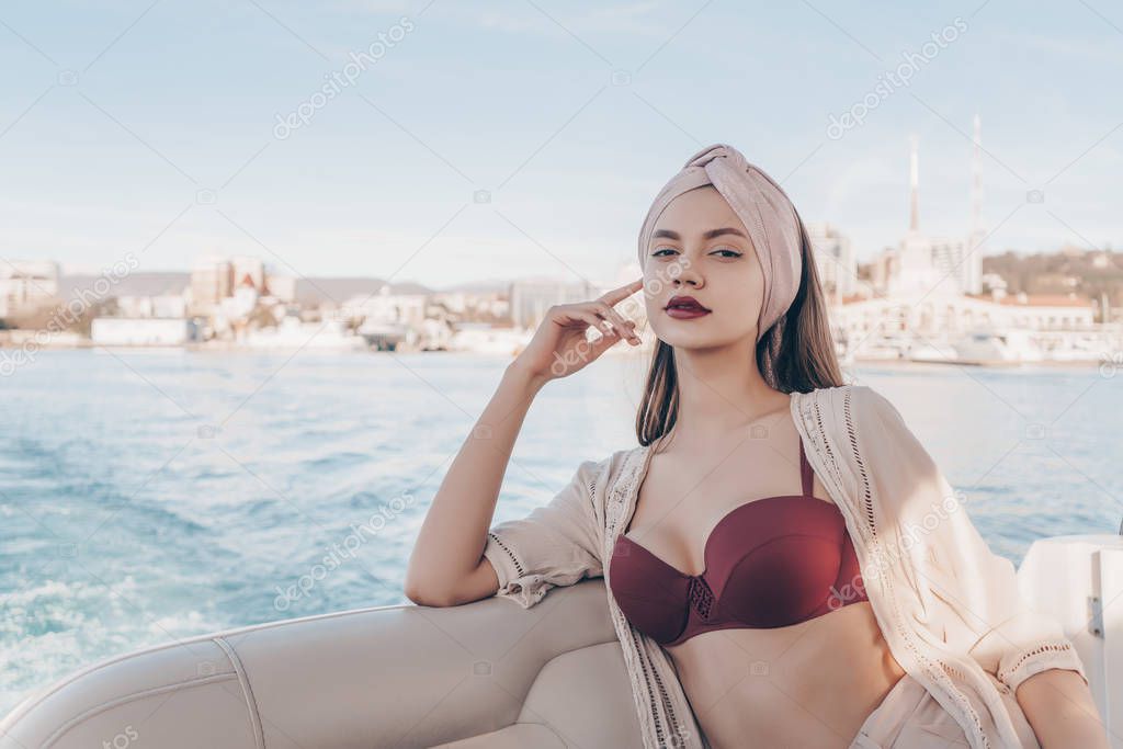 beautiful sexy girl in a swimsuit and with a headscarf on her head rests and relaxes on her white yacht, sails on the blue sea