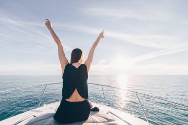 siyah yaz elbiseleri şık bir genç kız onun beyaz yatta oturur, güneşin sahiptir ve bırak, ellerini kaldırdı