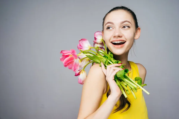 Joyful young woman in yellow dress holds a bouquet of fragrant pink flowers and smiles — Stock Photo, Image